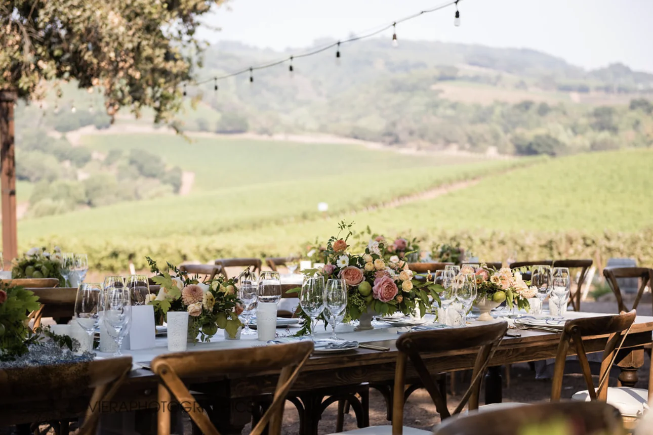 Long farm table set with flowers and glassware overlooking Kunde's vineyards at sunset