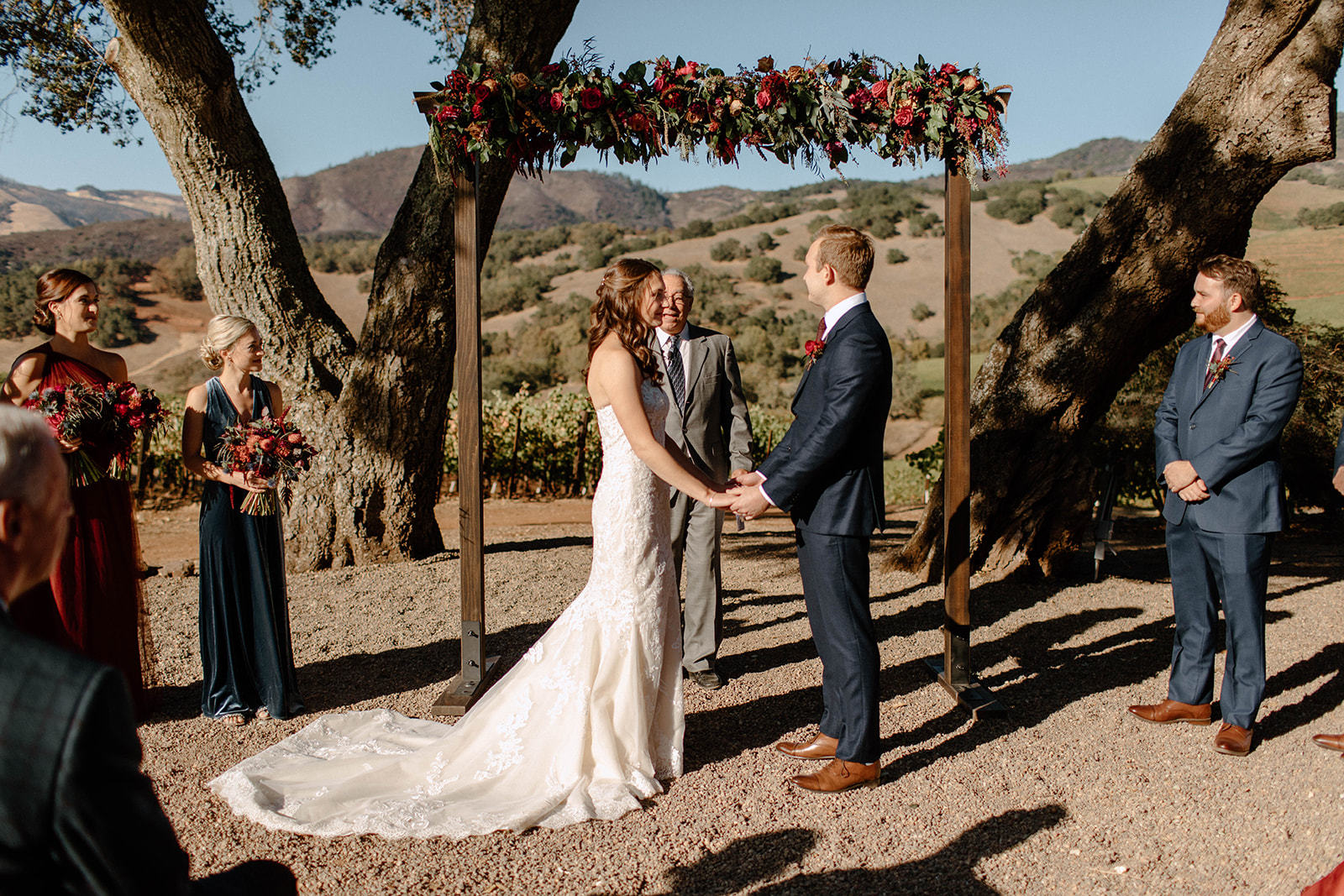 Bride and groom exchanging vows under a floral arbor framed by oaks at the Kunde estate